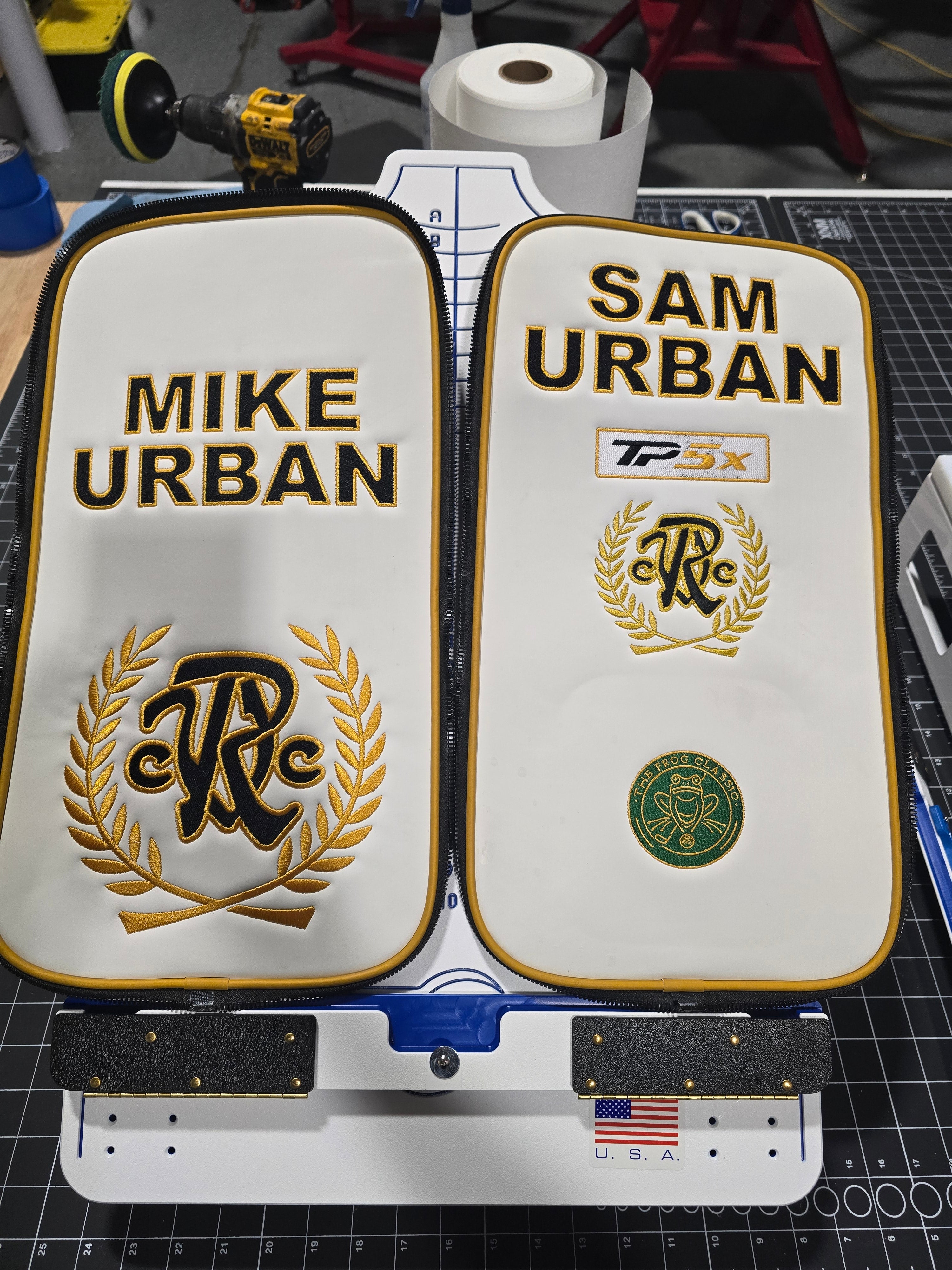 Two white golf bag covers with 'Mike Urban' and 'Sam Urban' branding on a workbench.