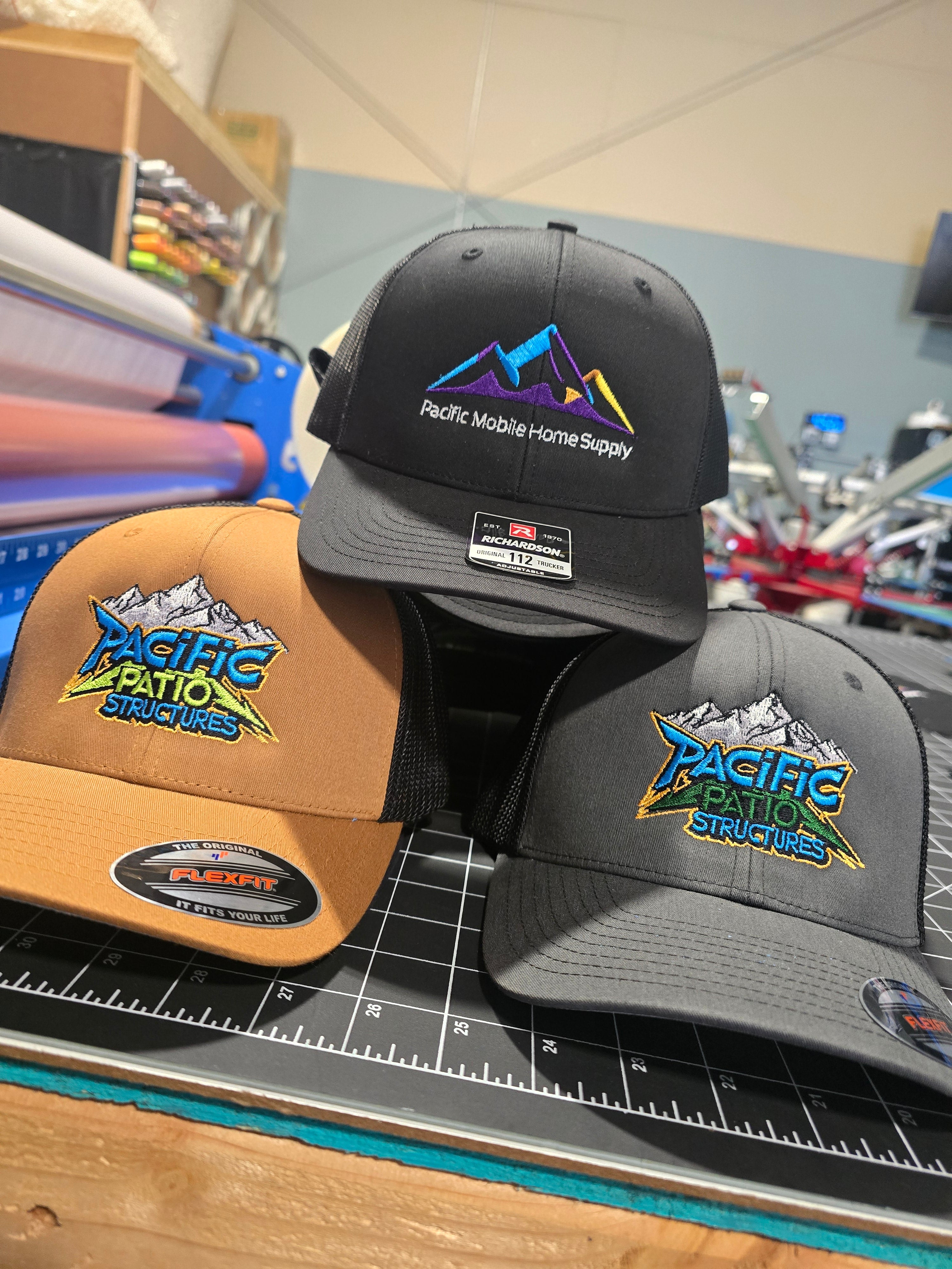Three hats with Pacific Patio Structures logo on a cutting mat