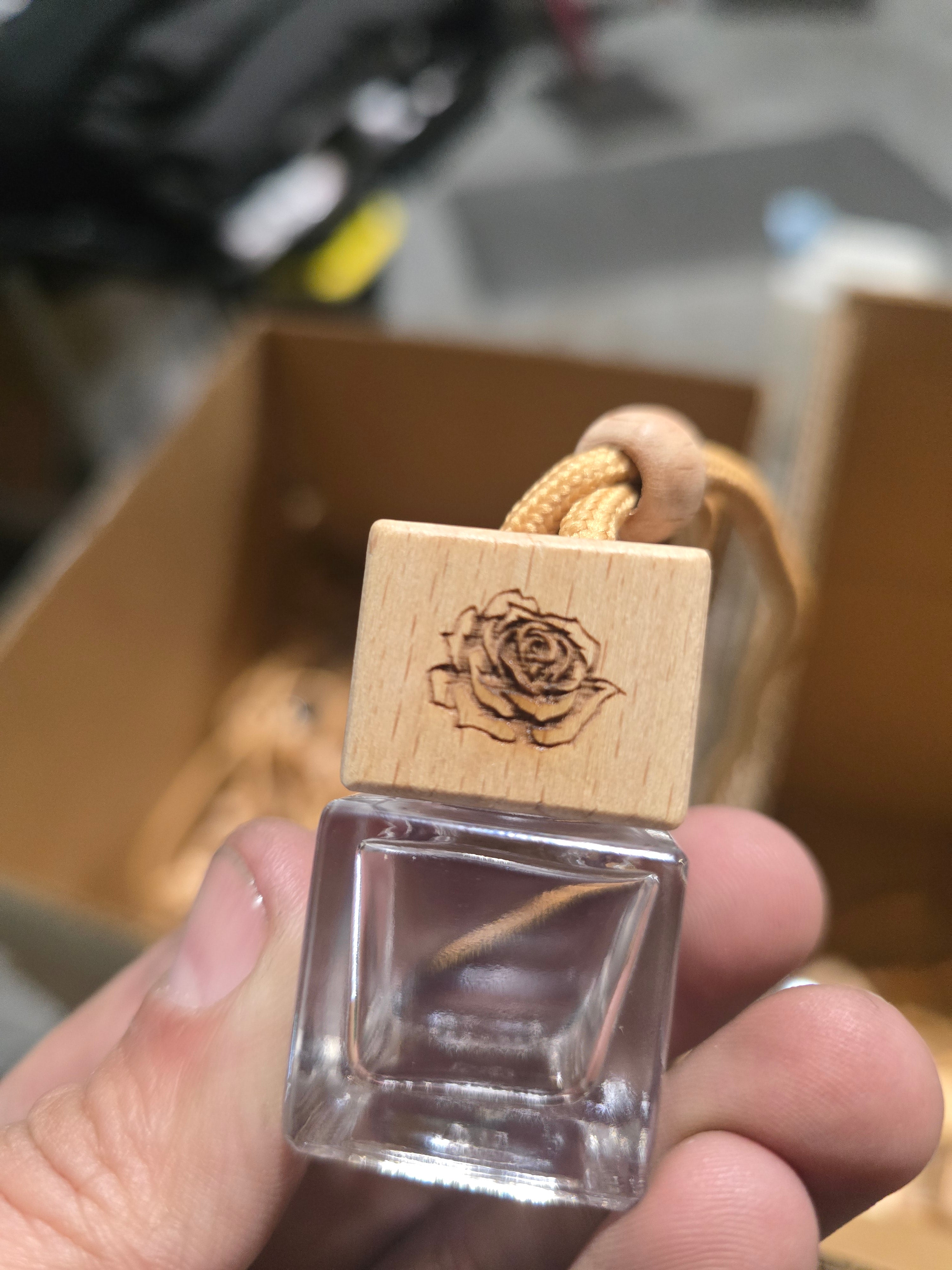 Clear glass container with wooden lid featuring a rose engraving, held by a hand.