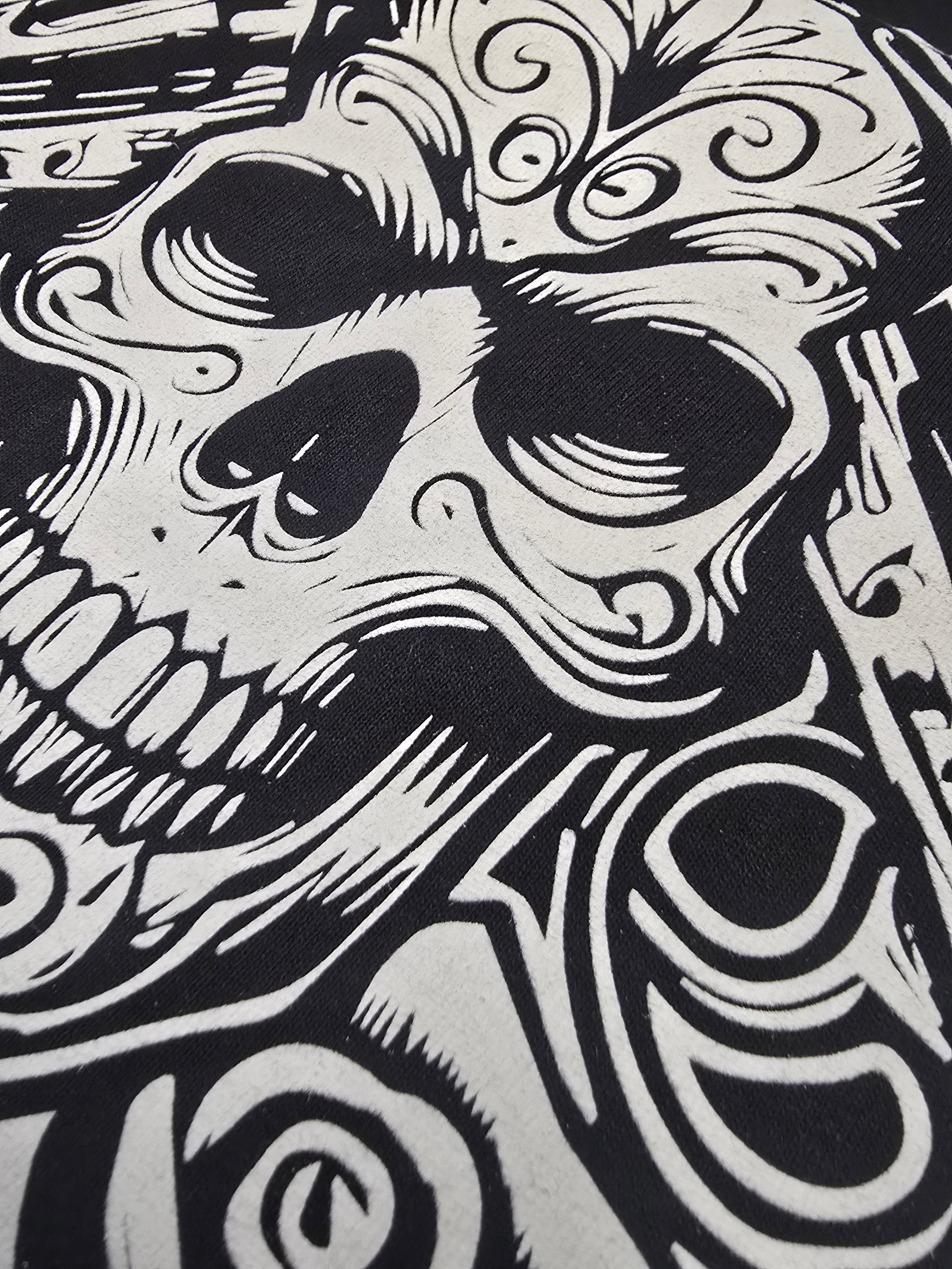 Black and white screen printed illustration of a stylized skull with intricate patterns.