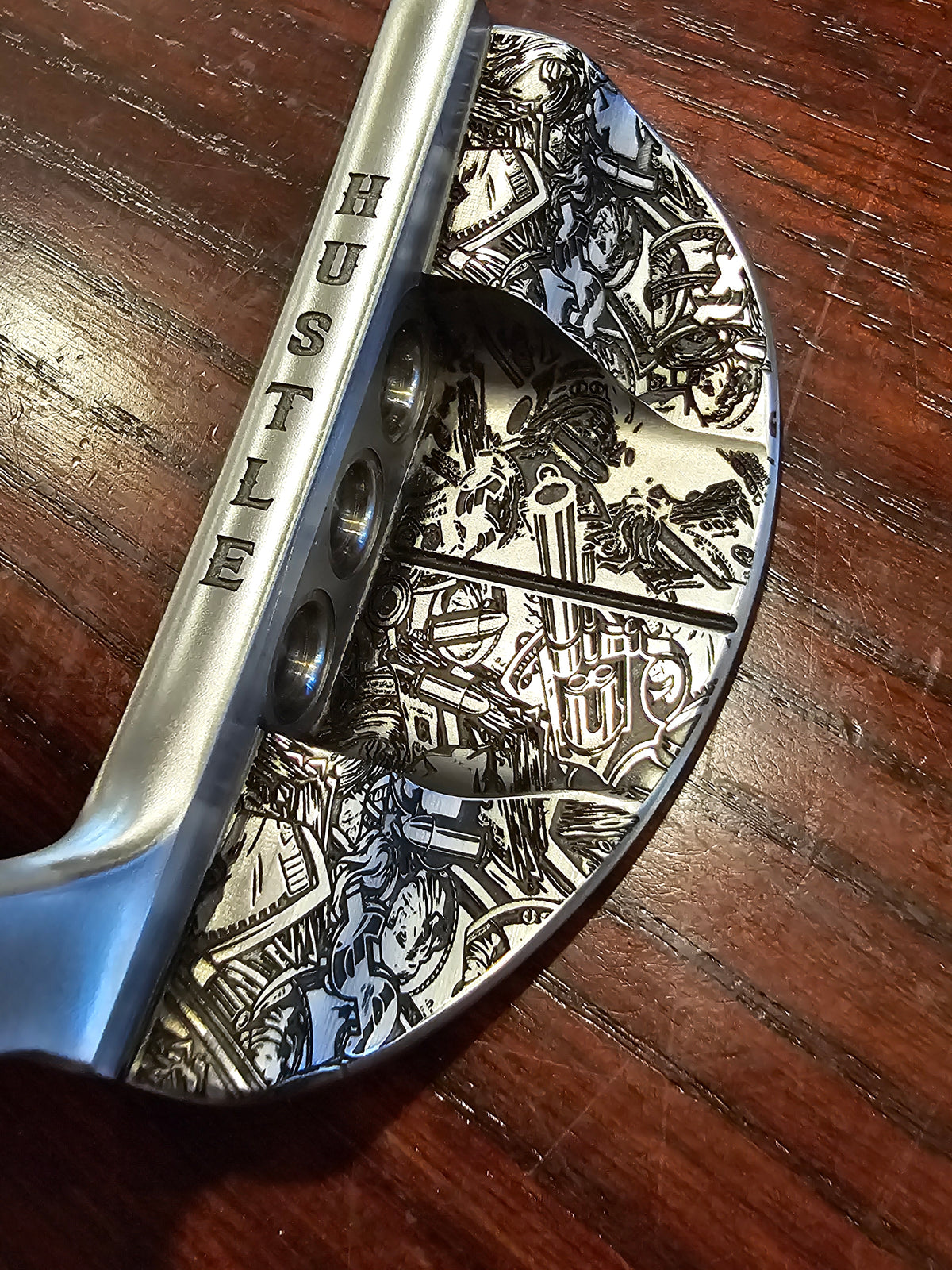 Metal golf club head with intricate designs laser engraved on a wooden surface