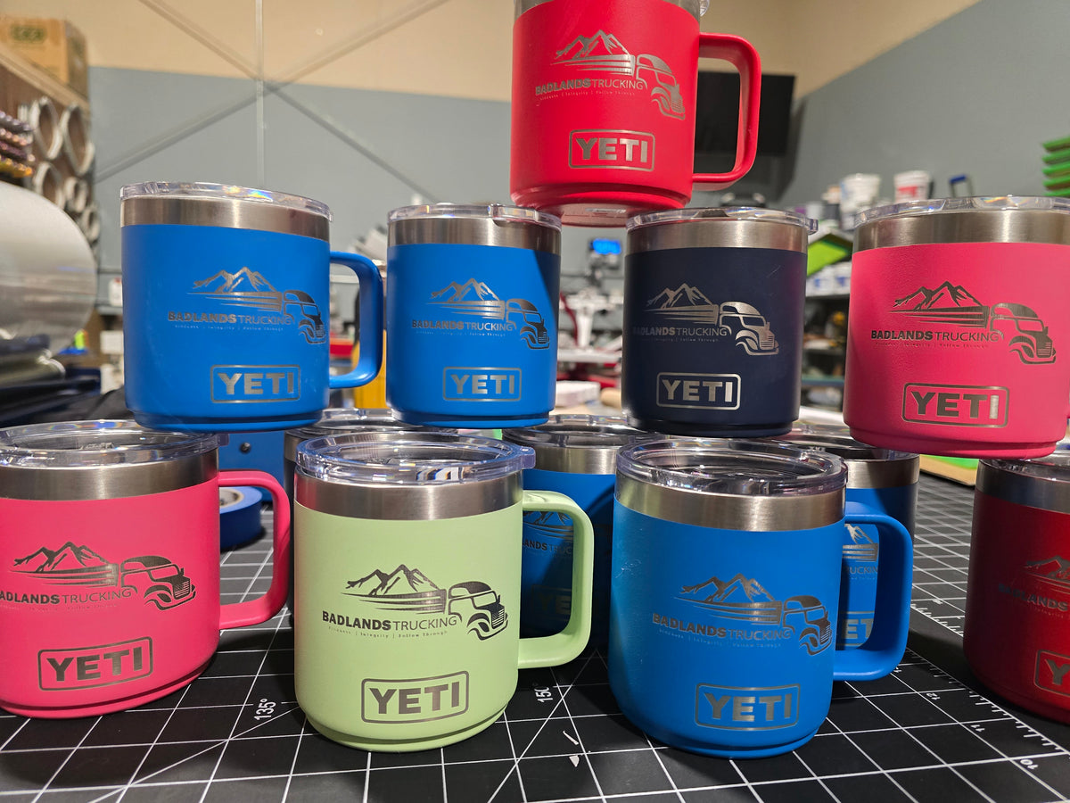 Collection of YETI branded mugs laser engraved in various colors on a checkered floor.