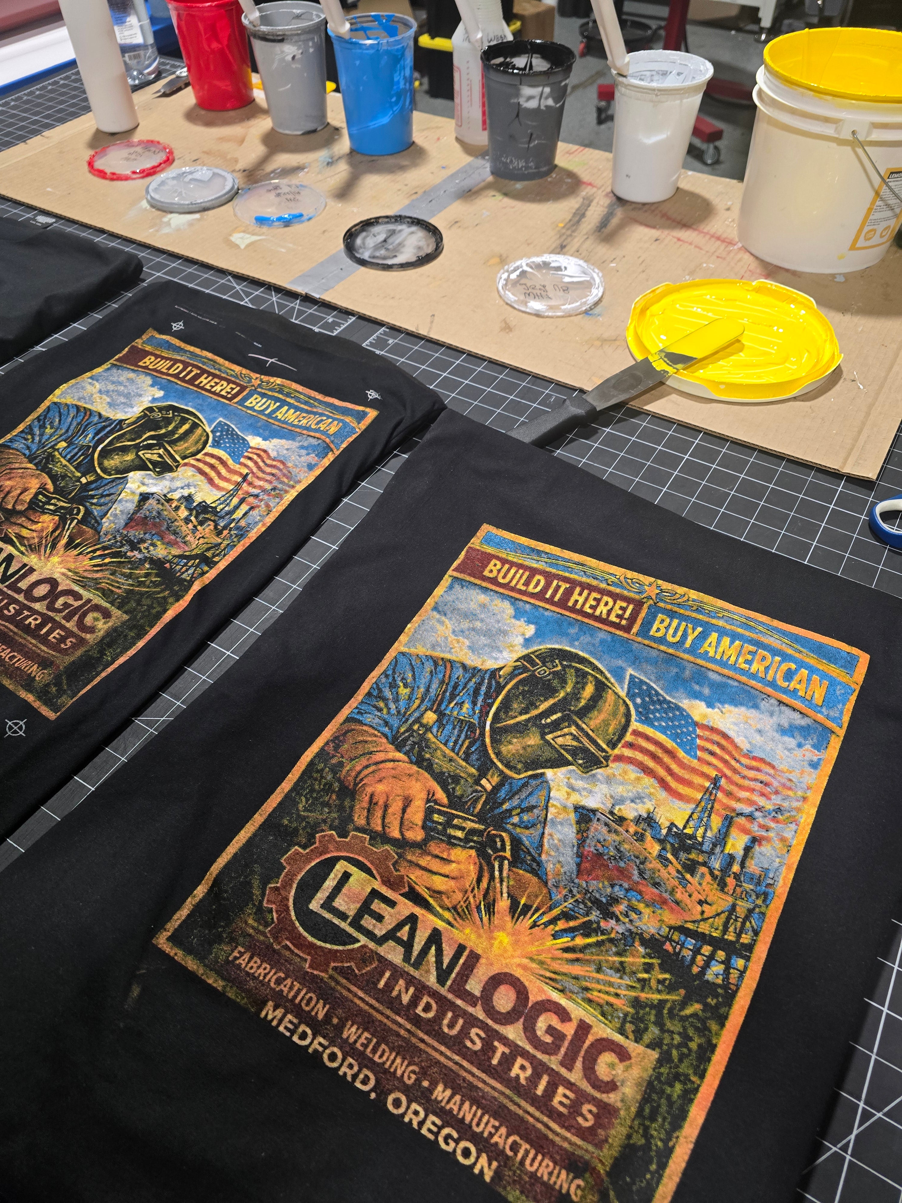 Black t-shirt with 'Cleanlogic Industries' graphic design screen printed on a workbench with tools.